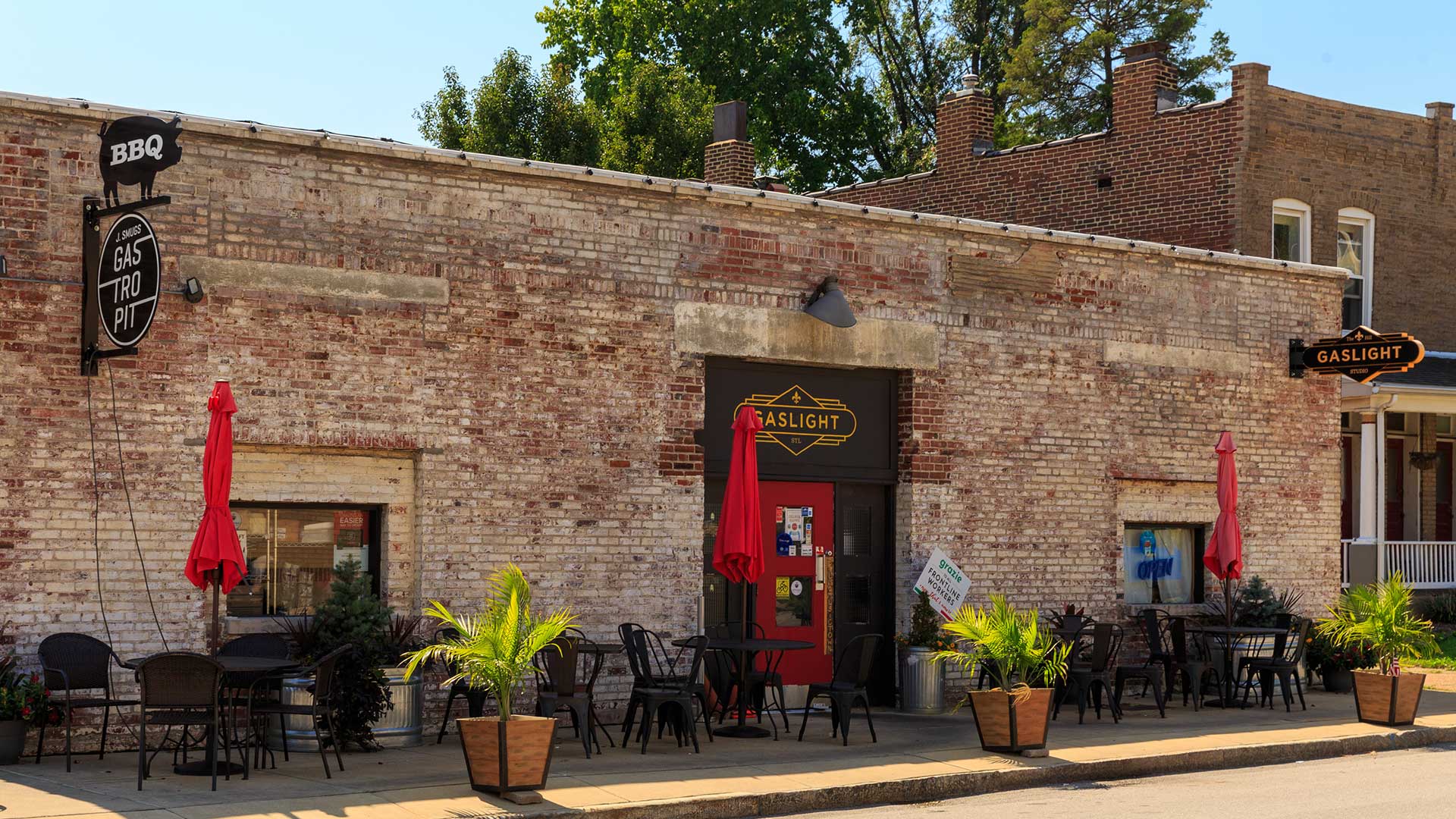A restaurant in a brick building with several black café tables out front with their umbrellas closed.