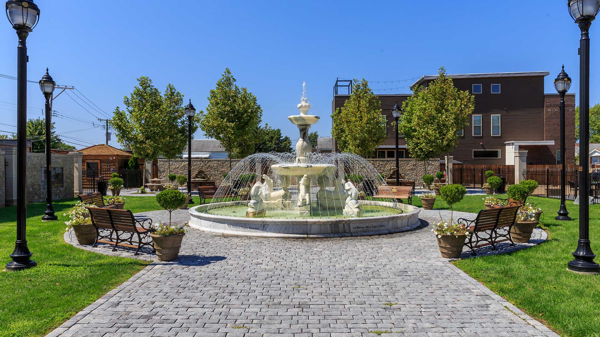An old, statuesque fountain with water flowing in a park in The Hill district of St. Louis on a clear, sunny day.