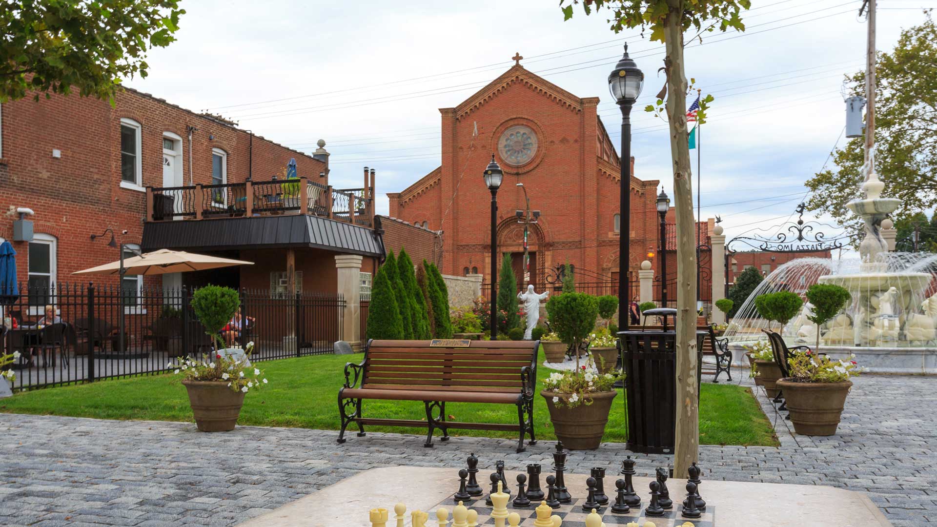 A chess board in a park with a fountain in the background and a red brick church further behind.