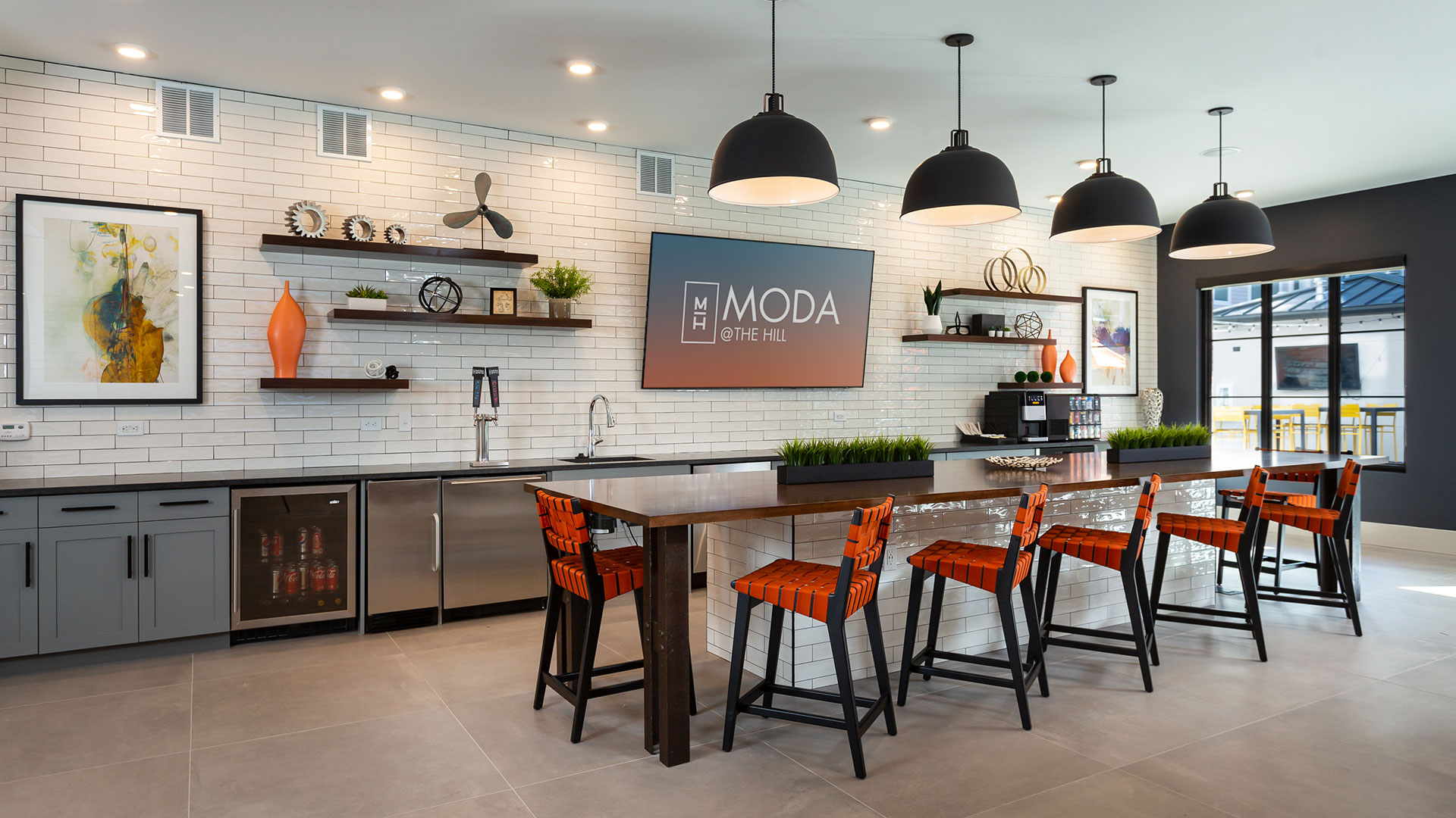 The catering kitchen at Moda at The Hill. A large bar sits in front of the kitchen that runs along the back wall. There are shelves with knick-knacks on them and a large screen television.