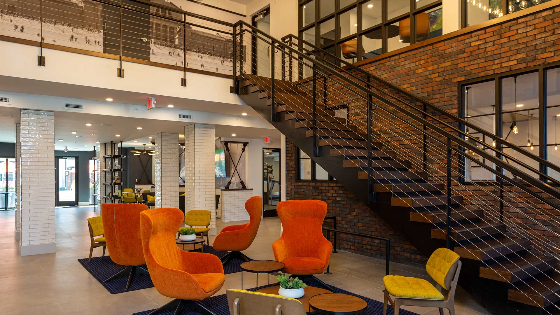 Standing near the front door in Moda at The Hill. Two lounge seating areas are up front with orange and yellow chairs. A stairway leads up along the right wall and off to the left is an open area with more lounge seating.