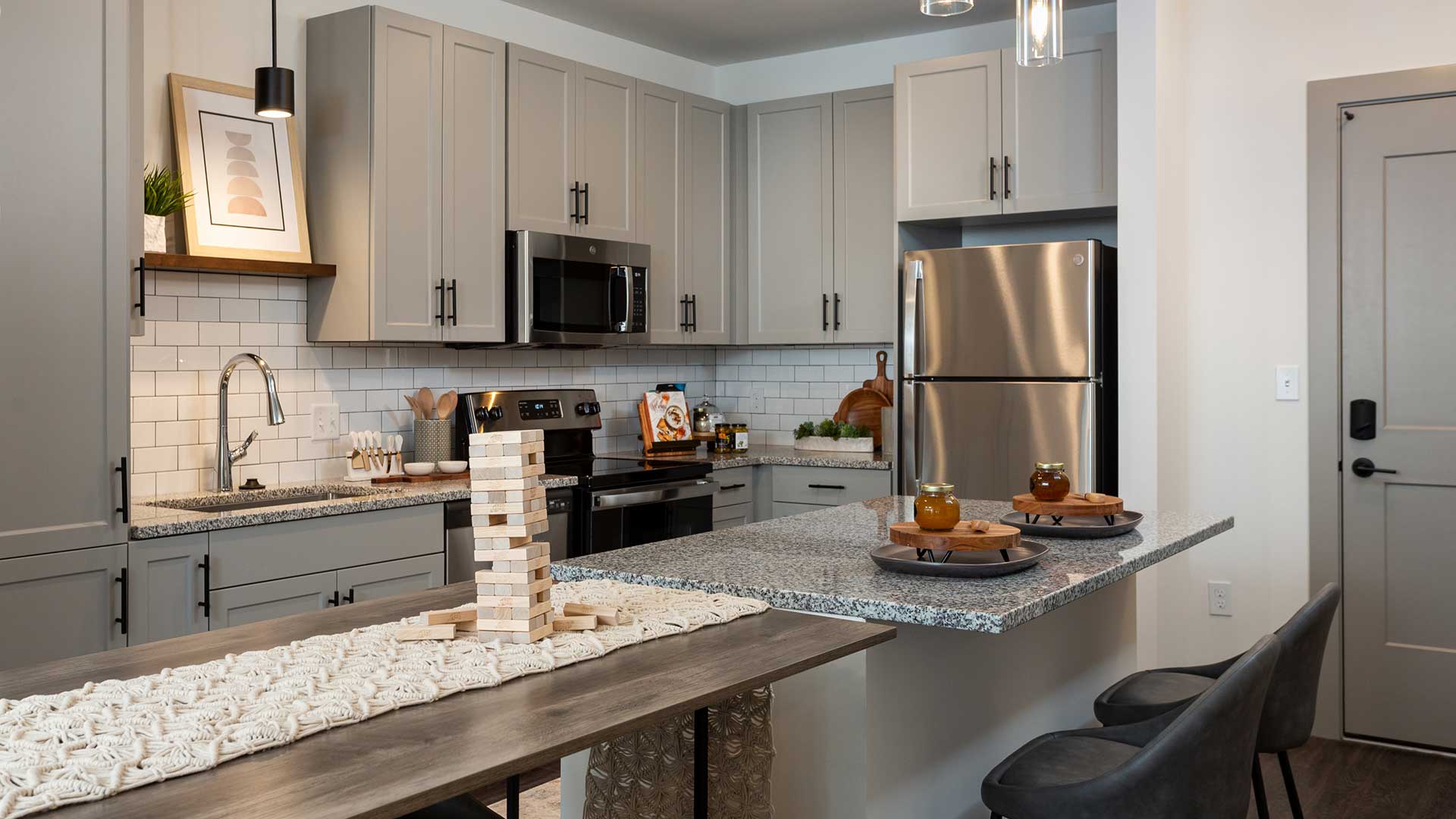 Looking into a kitchen from across the island countertop. There is a table with a block game in front. The kitchen has modern, grey cabinets and stainless steel appliances.